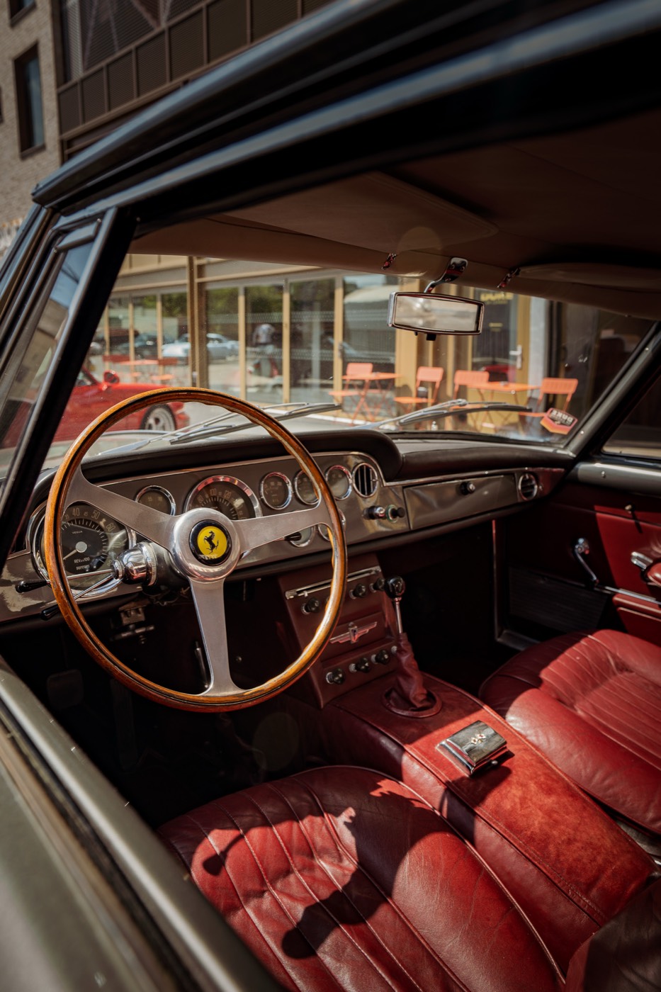 Vintage Ferrari interior with wood-rimmed steering wheel and red leather seats