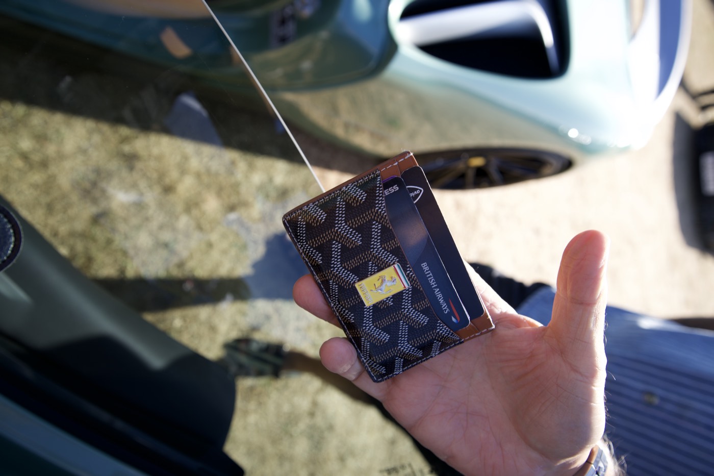 Hand holding a Goyard Ferrari card holder beside a green Ferrari SF90